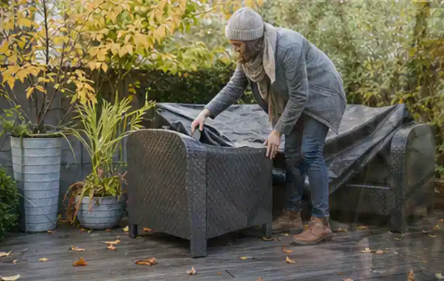 Person deckt Gartenmöbel vor der kalten Jahreszeit sorgfältig ab; Thema Sonnenschirme, Schwerpunkt Checkliste; Umsetzung.
