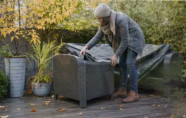 Person deckt Gartenmöbel vor der kalten Jahreszeit sorgfältig ab; Thema Sonnenschirme, Schwerpunkt Ersatzteile; Umsetzung.