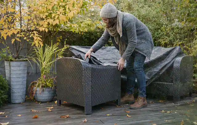 Person deckt Gartenmöbel vor der kalten Jahreszeit sorgfältig ab; Thema Sonnenschirme, Schwerpunkt Kaufberatung; Kontrolle.