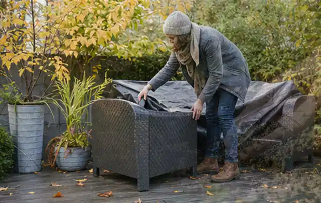 Person deckt Gartenmöbel vor der kalten Jahreszeit sorgfältig ab; Thema Sonnenschirme, Schwerpunkt Reparatur; Ausgangslage.