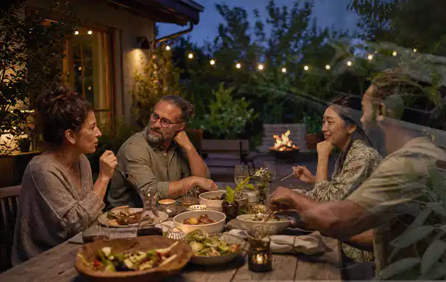 Menschen verbringen einen ruhigen Abend an einem Sitzplatz im Garten; Thema Sonnenschirme, Schwerpunkt Sicherheit; Umsetzung.