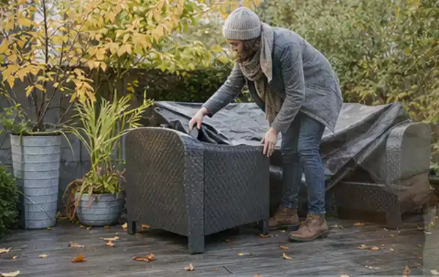 Person deckt Gartenmöbel vor der kalten Jahreszeit sorgfältig ab; Thema Sonnenschirme, Schwerpunkt Systemvergleich; Ausgangslage.