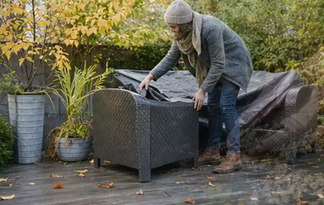 Person deckt Gartenmöbel vor der kalten Jahreszeit sorgfältig ab; Thema Sonnenschirme, Schwerpunkt Wartung; Ausgangslage.