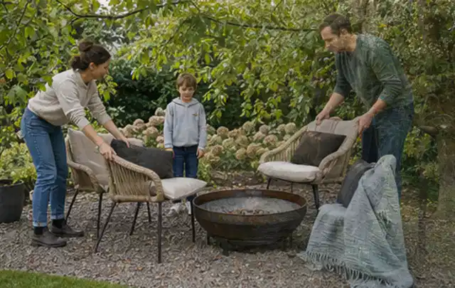 Familie stellt wetterfeste Sessel an einem geschützten Sitzplatz im Garten auf; Thema Sonnenschirme, Schwerpunkt Wartung; Kontrolle.