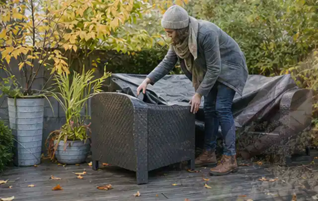 Person deckt Gartenmöbel vor der kalten Jahreszeit sorgfältig ab; Thema Sonnenschirme, Schwerpunkt Winterlager; Ergebnis.