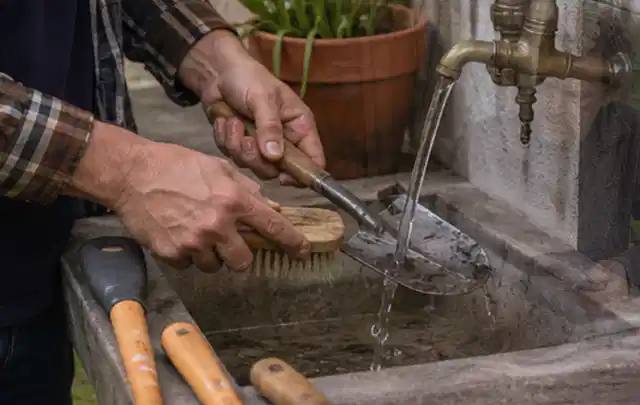 Hände reinigen gebrauchte Gartengeräte mit Bürste und Wasser am Außenbecken; Thema Stihl iMow, Schwerpunkt Gärten mit kleiner Fläche; Ergebnis.