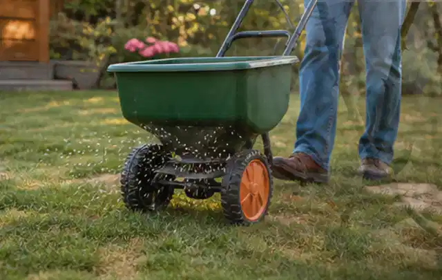 Person verteilt Rasensamen mit einem Streuwagen auf einer lückigen Fläche; Thema Stihl iMow, Schwerpunkt Kosten; Kontrolle.
