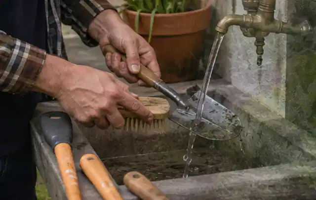 Hände reinigen gebrauchte Gartengeräte mit Bürste und Wasser am Außenbecken; Thema Stihl iMow, Schwerpunkt Mähroboter; Kontrolle.