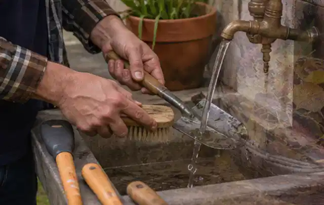Hände reinigen gebrauchte Gartengeräte mit Bürste und Wasser am Außenbecken; Thema Stihl iMow, Schwerpunkt Reparatur; Umsetzung.