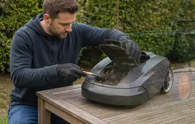 Person wartet einen geöffneten Mähroboter auf einem stabilen Gartentisch; Thema Vertikutierer, Schwerpunkt Kaufberatung; Umsetzung.