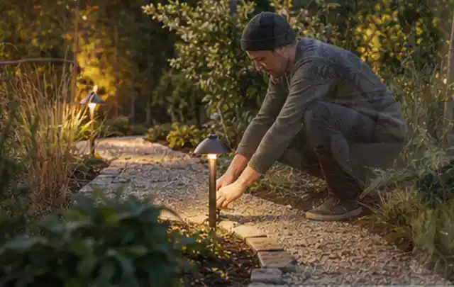 Person richtet eine niedrige warm leuchtende Gartenlampe am Kiesweg aus; Thema Whirlpools, Schwerpunkt Fehlerhilfe; Ergebnis.