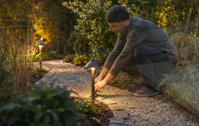 Person richtet eine niedrige warm leuchtende Gartenlampe am Kiesweg aus; Thema Whirlpools, Schwerpunkt Kaufberatung; Kontrolle.