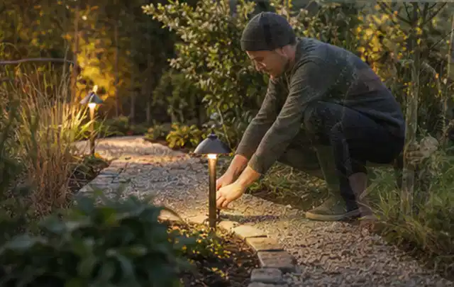 Person richtet eine niedrige warm leuchtende Gartenlampe am Kiesweg aus; Thema Whirlpools, Schwerpunkt Outdoor Freizeit; Ausgangslage.