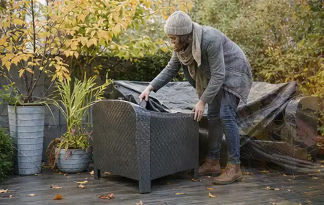 Person deckt Gartenmöbel vor der kalten Jahreszeit sorgfältig ab; Thema Whirlpools, Schwerpunkt Vergleich; Praxisalltag.