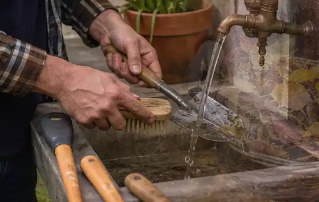 Hände reinigen gebrauchte Gartengeräte mit Bürste und Wasser am Außenbecken; Thema Worx Landroid, Schwerpunkt Gärten mit kleiner Fläche; Umsetzung.
