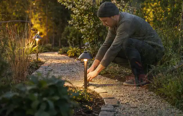 Person richtet eine niedrige warm leuchtende Gartenlampe am Kiesweg aus; Thema Worx Landroid, Schwerpunkt Kaufberatung; Ausgangslage.