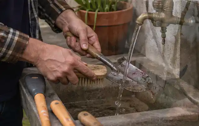 Hände reinigen gebrauchte Gartengeräte mit Bürste und Wasser am Außenbecken; Thema Worx Landroid, Schwerpunkt Mähroboter; Ergebnis.