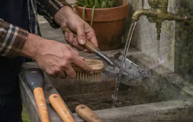Hände reinigen gebrauchte Gartengeräte mit Bürste und Wasser am Außenbecken; Thema Worx Landroid, Schwerpunkt Winterlager; Umsetzung.