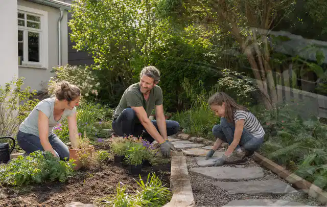 Familie geht auf einem Weg durch einen abwechslungsreich gestalteten Garten; Thema WPC Sichtschutz, Schwerpunkt Materialwahl; Praxisalltag.