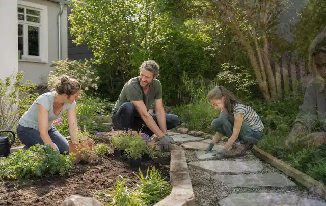 Familie geht auf einem Weg durch einen abwechslungsreich gestalteten Garten; Thema WPC Sichtschutz, Schwerpunkt Pflege; Umsetzung.